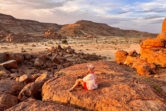 Frau sitzt auf einem Felsen in Namibia und genie&szlig;t die Aussicht auf rote Felsen